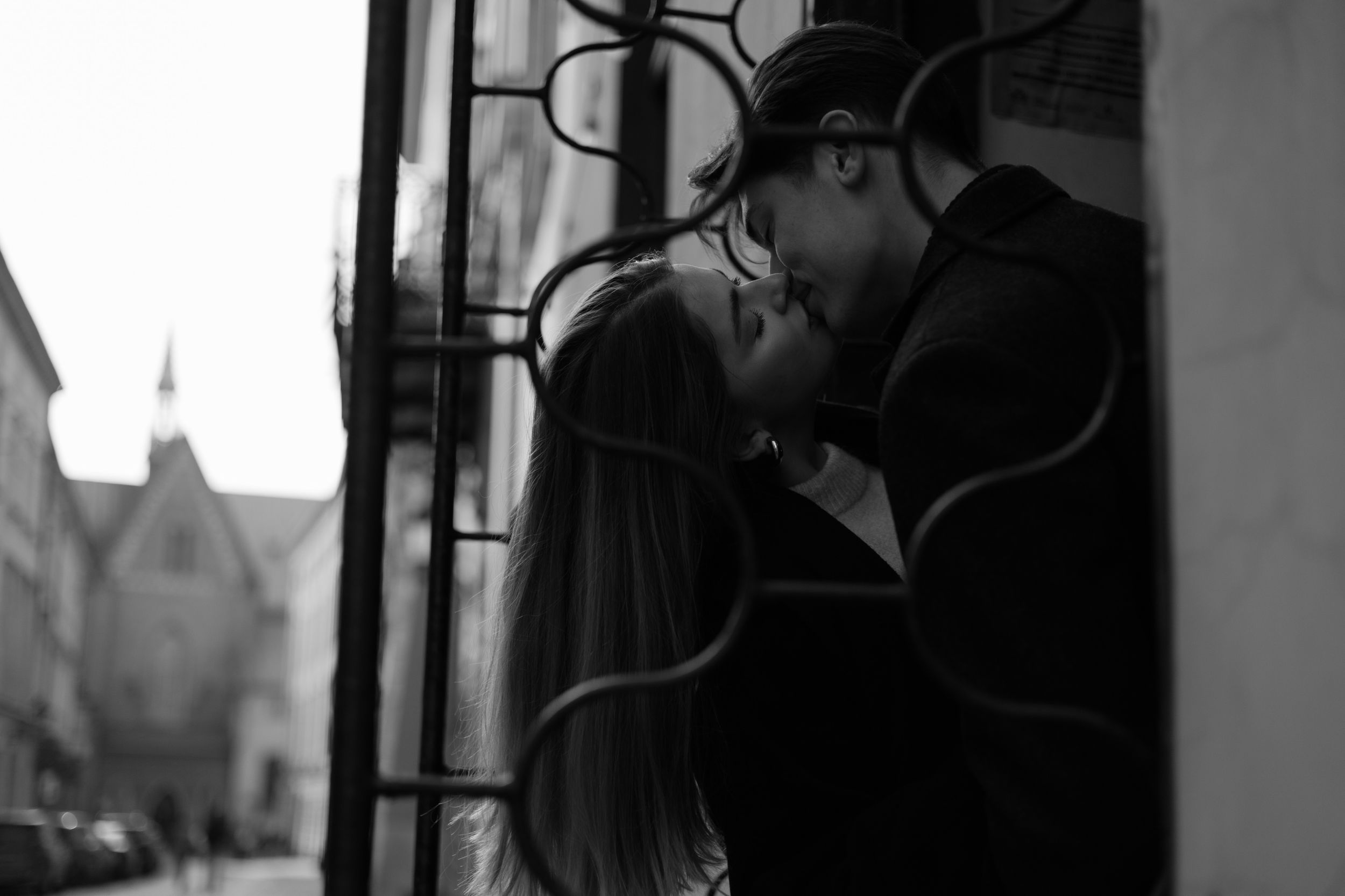 A romantic black and white image of a couple embracing near decorative iron window bars.