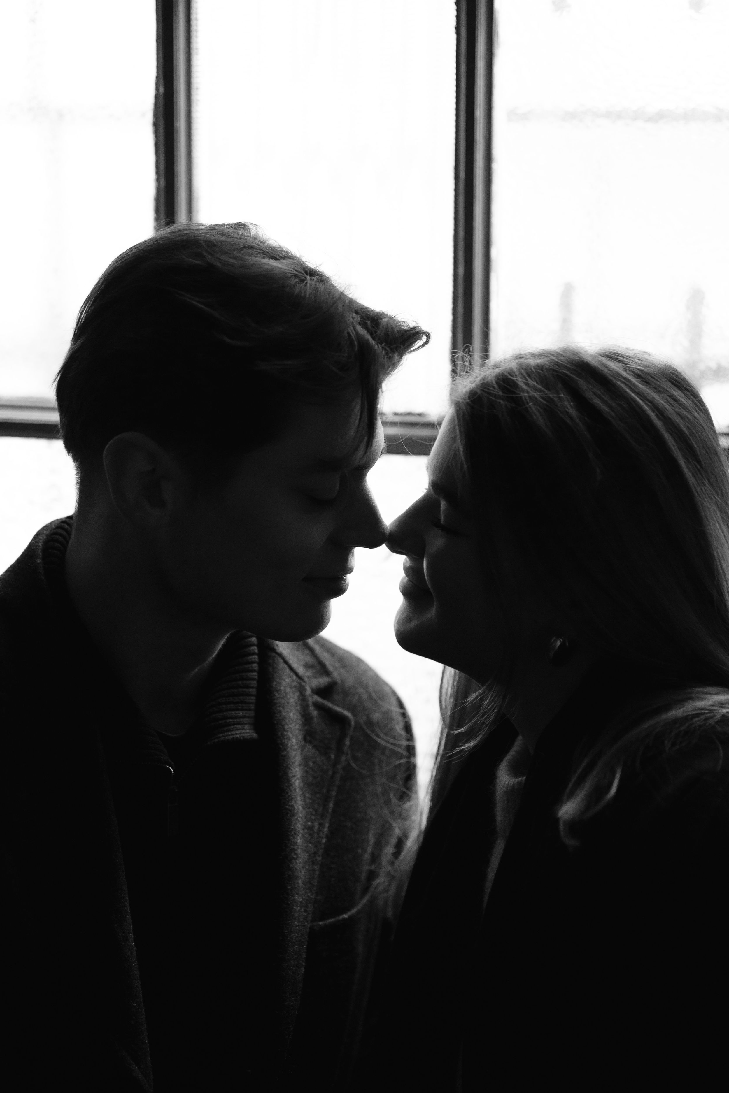 Silhouetted couple in tender moment by window in black and white romantic photograph.