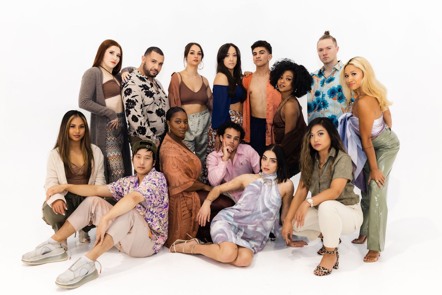 A diverse group of people pose together in casual clothing and neutral tones against a white background.