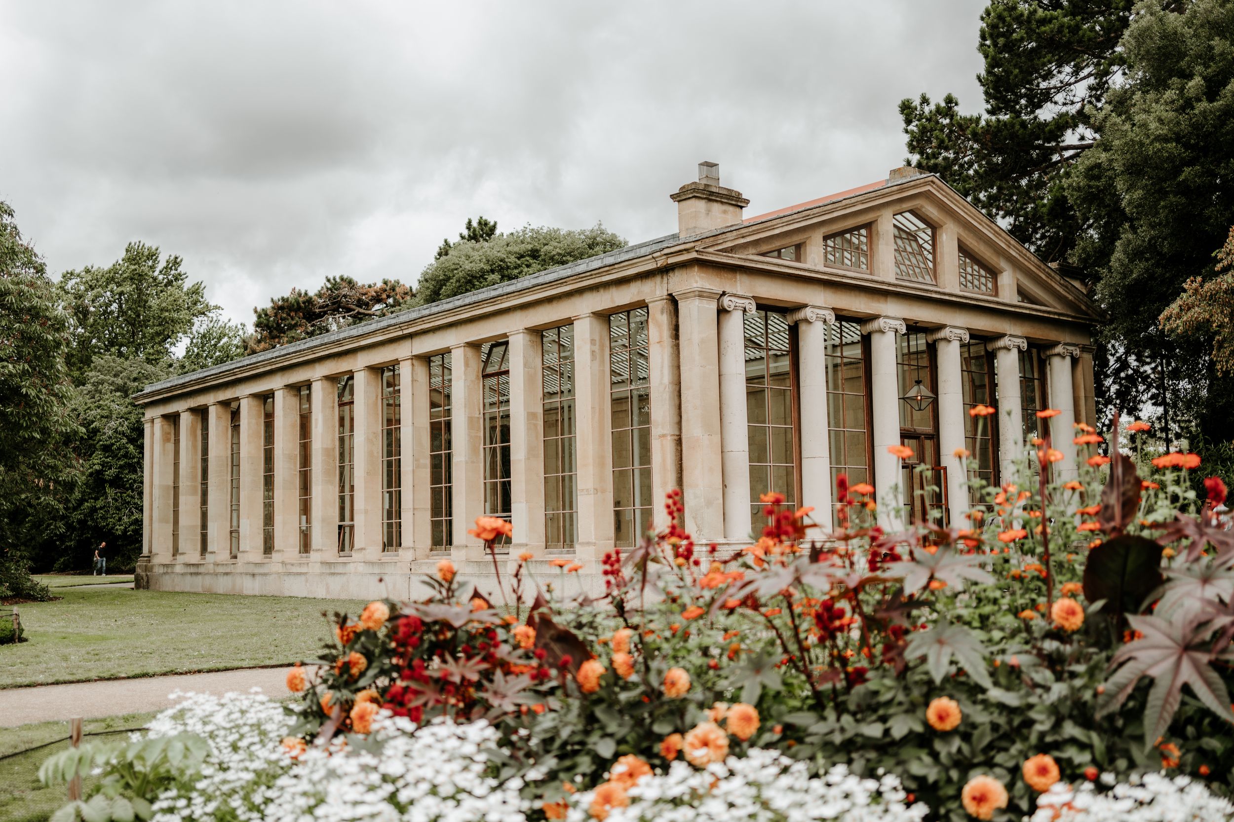 Neoclassical building with grand white columns and ornate architecture surrounded by colorful flower gardens and landscaping.
