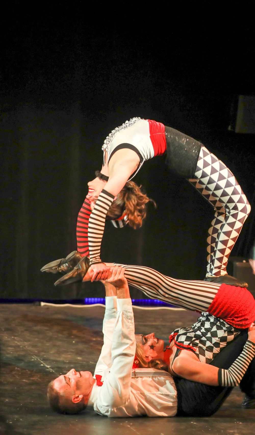 Circus acrobats perform a dramatic balancing act featuring geometric patterned costumes in red and black.