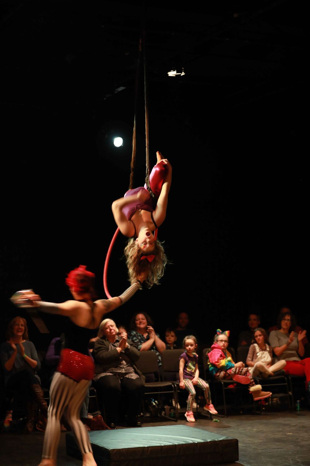 Circus performers in red costumes execute an impressive aerial dance routine as an audience watches from the side.