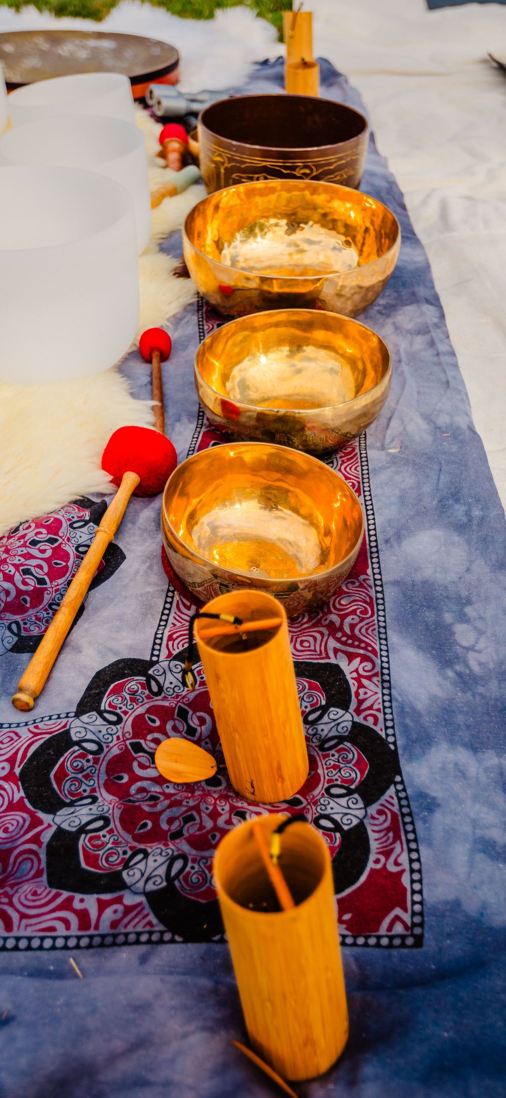 Tibetan singing bowls and meditation tools arranged on a decorative cloth with wooden mallets and bamboo accessories.