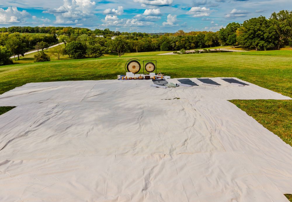 Aerial view of white event tent being set up in a green field with archery targets visible under blue cloudy skies.