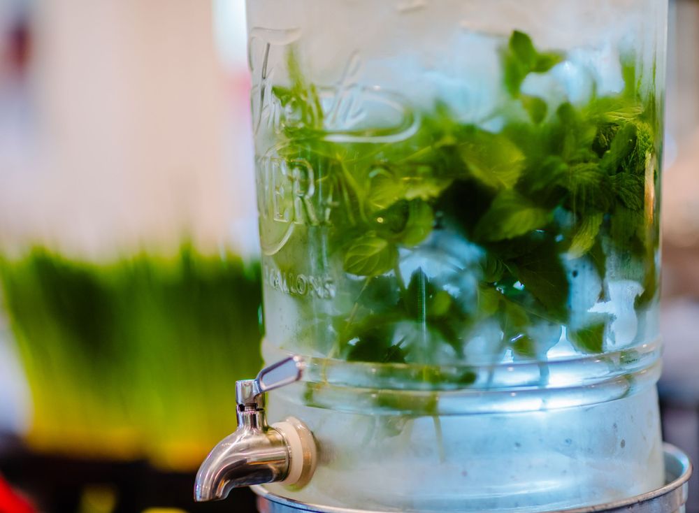Fresh mint leaves steeping in a glass beverage dispenser with spigot against blurred background.
