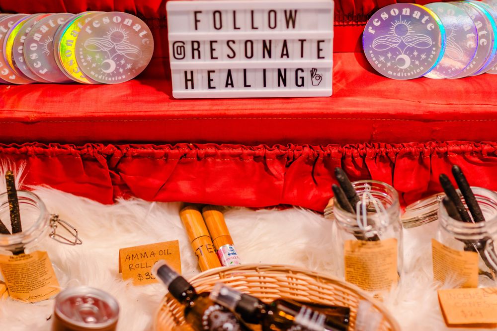 A collection of healing crystals and spiritual items displayed on a red surface with a sign reading 'Follow Resonate Healing'.