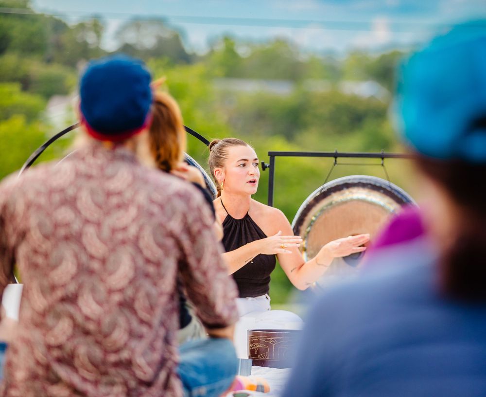 Outdoor sound healing session with gongs and singing bowls surrounded by attendees on a sunny day.