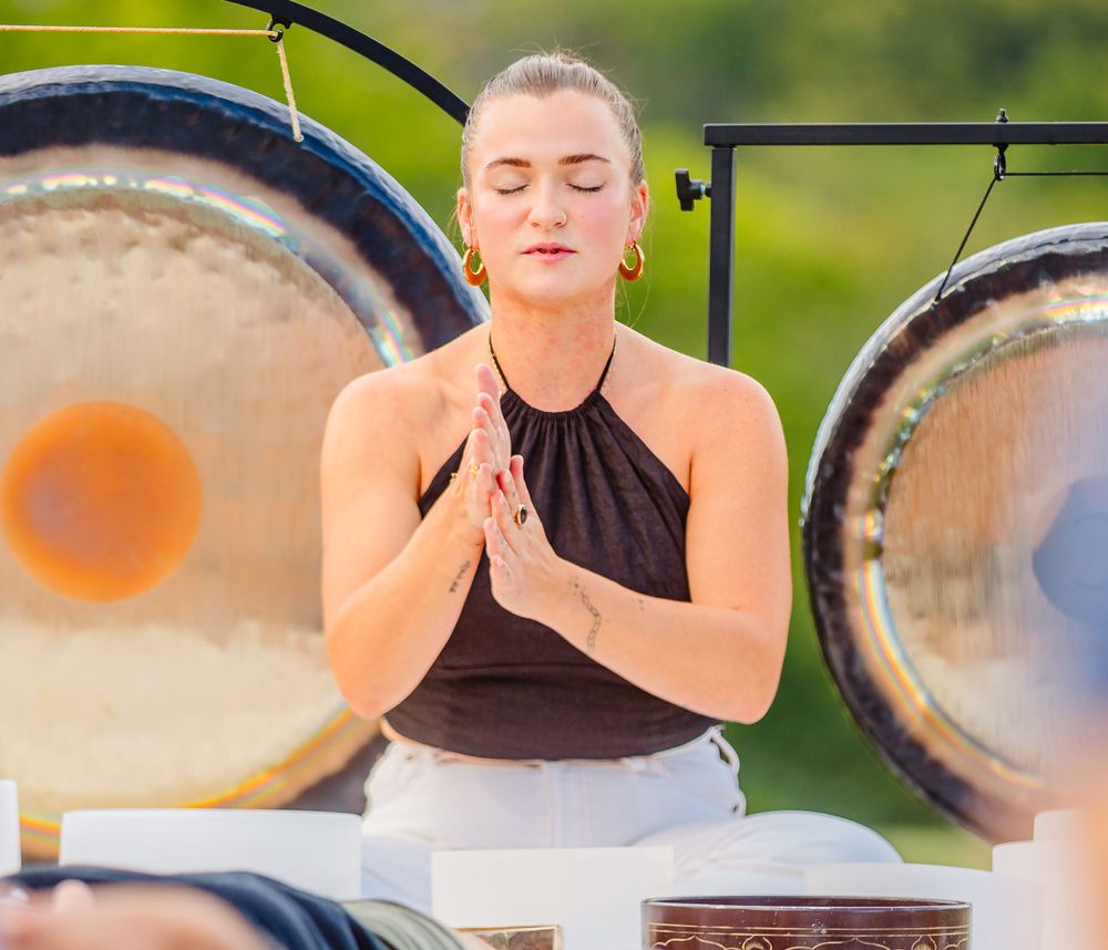 Meditating at a sound healing ceremony with large gongs in an outdoor setting.