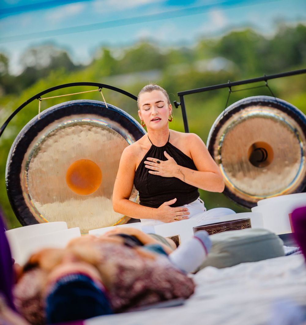 Someone practicing mindfulness and meditation at an outdoor sound healing session with large gongs in the background.