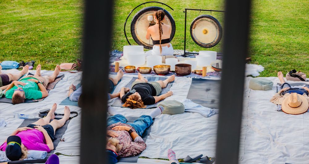 People lying on blankets for an outdoor sound healing ceremony with singing bowls on the grass.
