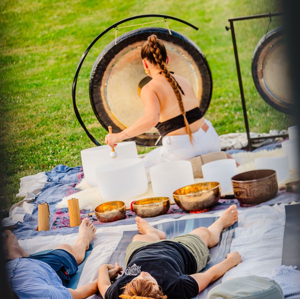 Sound healing setup with multiple singing bowls arranged on white cloth outdoors.