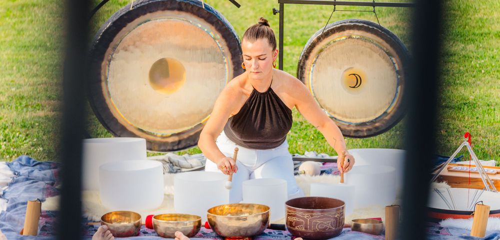 A sound healing practitioner sits at a table with Tibetan singing bowls for a healing ceremony.