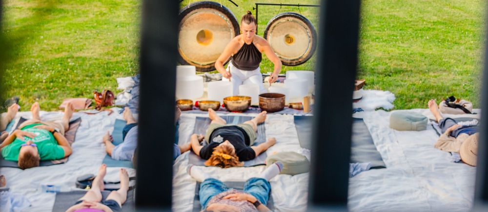 People lying down for a sound bath meditation session with gongs visible through a window.