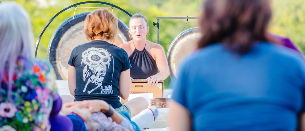 Outdoor sound healing workshop with gongs and participants gathered on grass.
