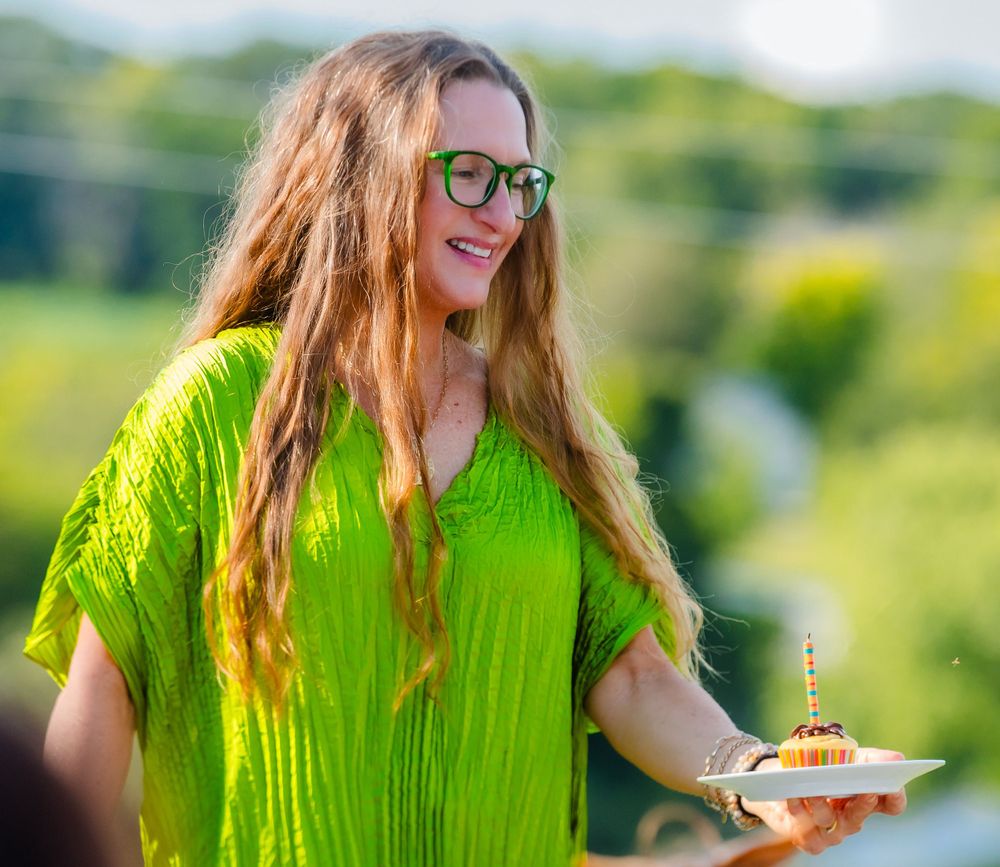 A person in a bright lime green dress holding a small plate outdoors with lush greenery in the background.