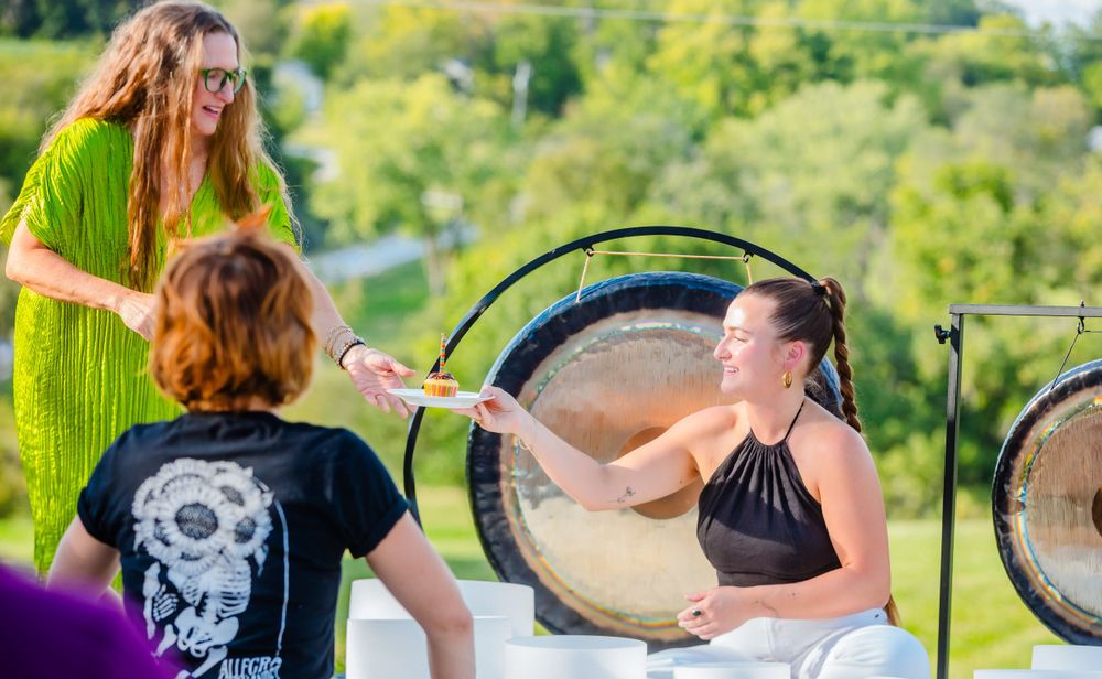 Wellness practitioners interact during an outdoor sound healing session with large gongs and singing bowls.