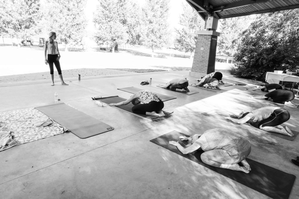 A black and white image showing people sleeping under a covered area with yoga mats and belongings spread out.