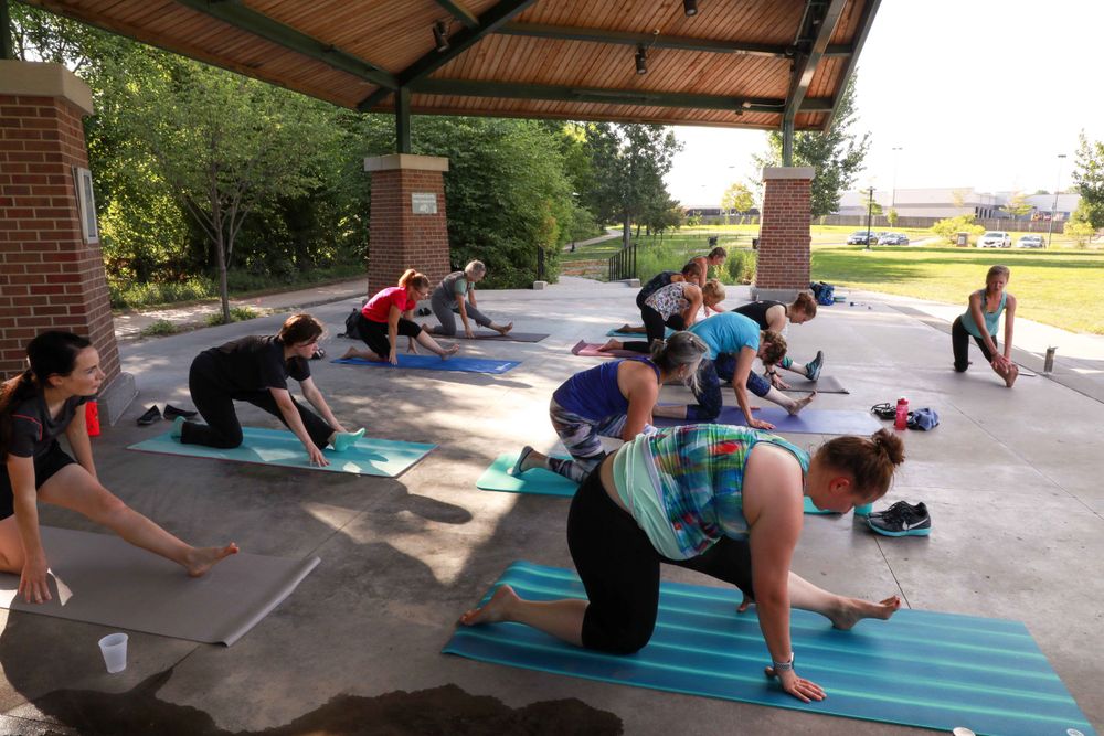 A group of people exercising together on blue yoga mats under a covered outdoor pavilion.