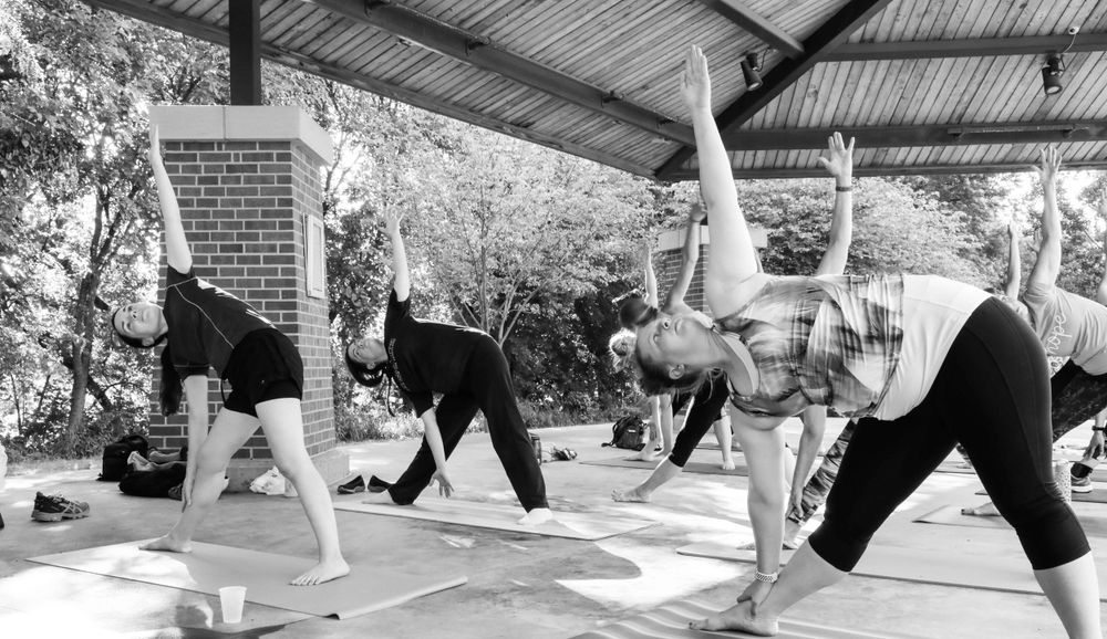Black and white photo of yoga students practicing triangle pose during an outdoor class on a covered patio.