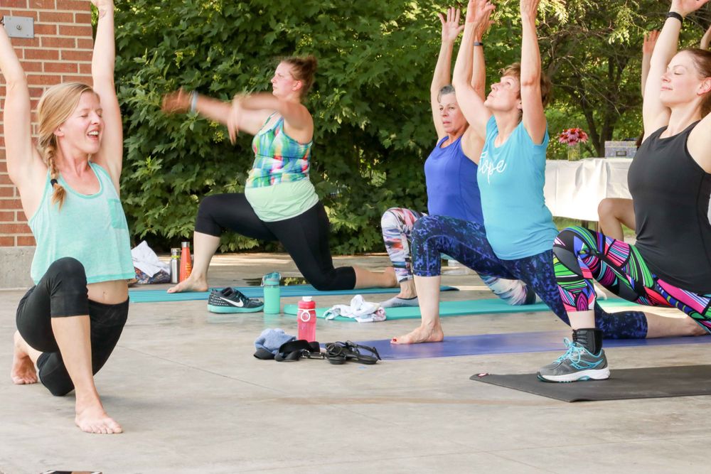 Outdoor fitness class participants perform lunges on exercise mats during a group workout session.