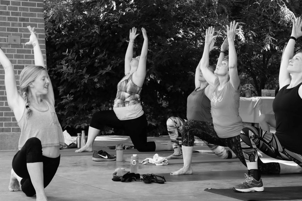 A group of people practicing yoga in an outdoor setting, striking crescent moon poses in black and white.