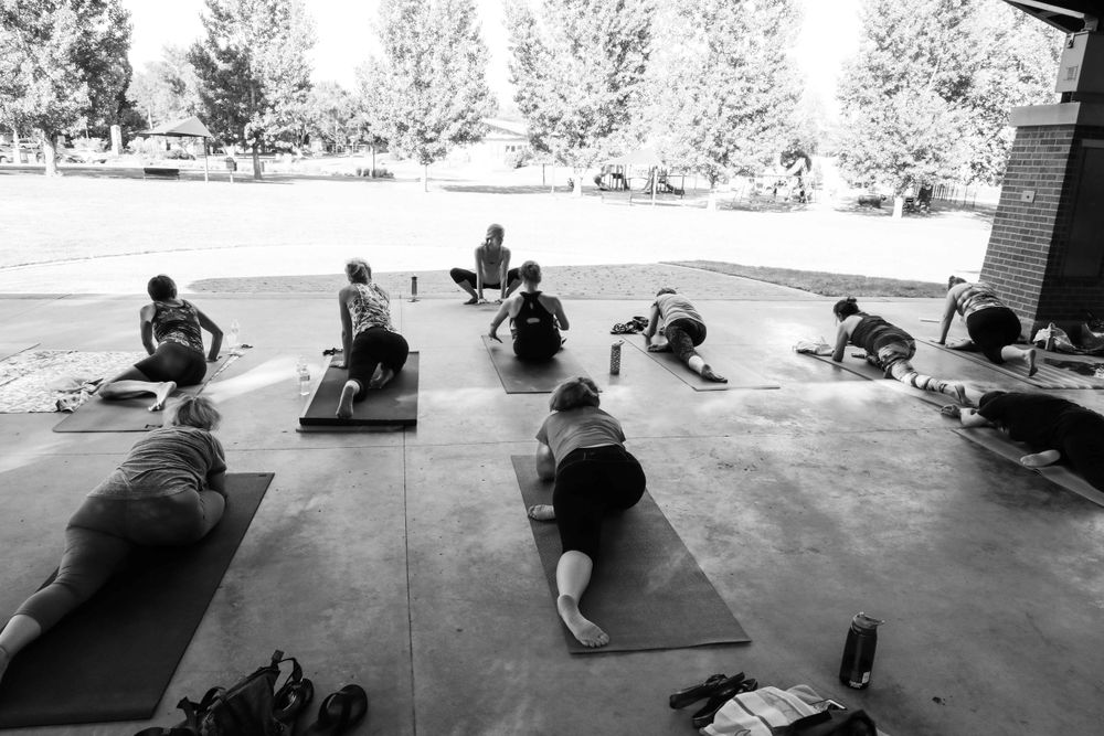 Group fitness class participants doing stretching exercises on yoga mats in a covered outdoor pavilion area.