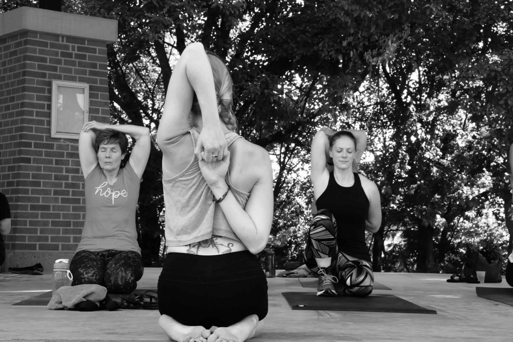 Three people practice yoga poses outdoors on mats during a black and white outdoor fitness session.