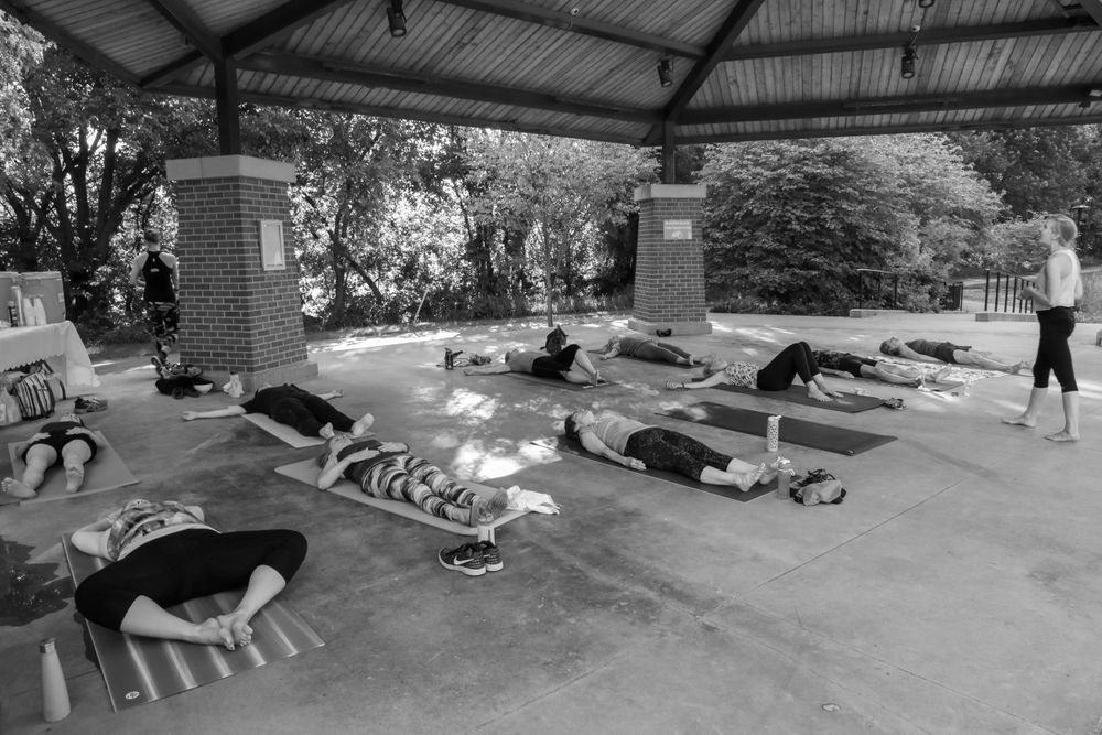 A black and white photo of yoga practitioners lying in savasana pose under a covered pavilion during a class.