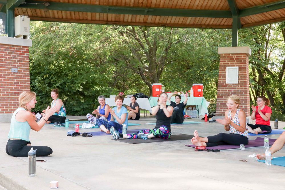 Group of people practicing yoga and meditation together on yoga mats under an outdoor pavilion structure.