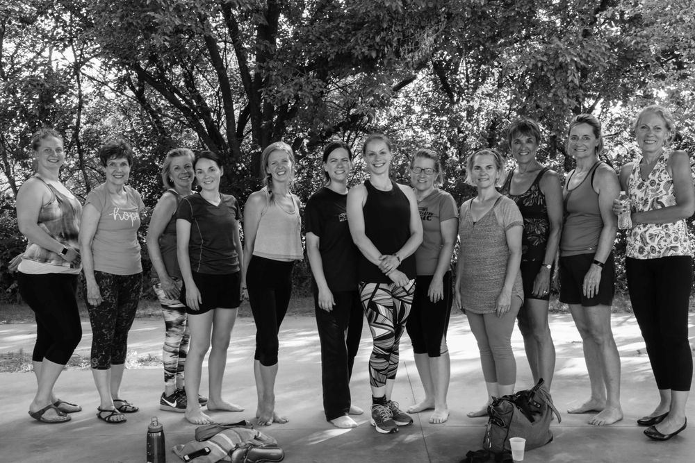 A black and white photograph of a fitness group gathered outdoors under trees in workout attire.