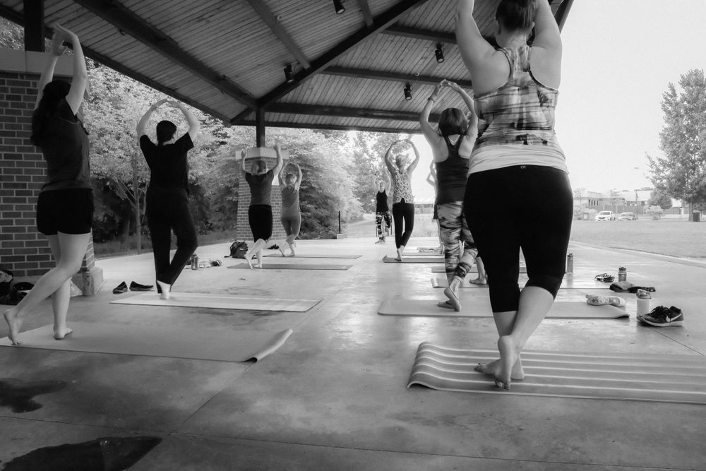 People practicing yoga in a covered outdoor setting during a group fitness class, captured in black and white.
