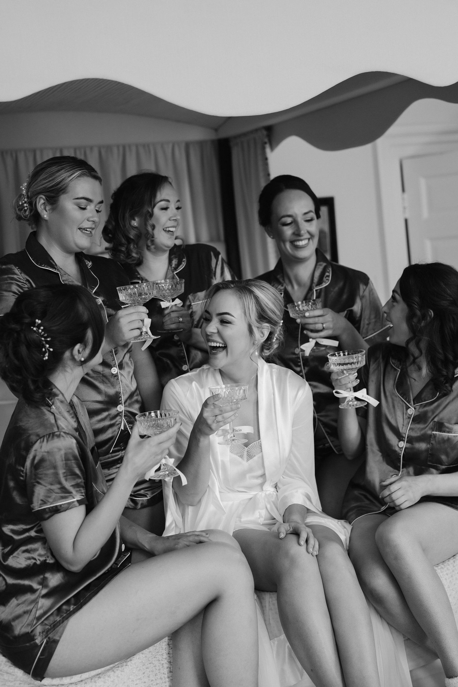bride and bridesmaids drinking champagne sat on the bed at Iscoyd park