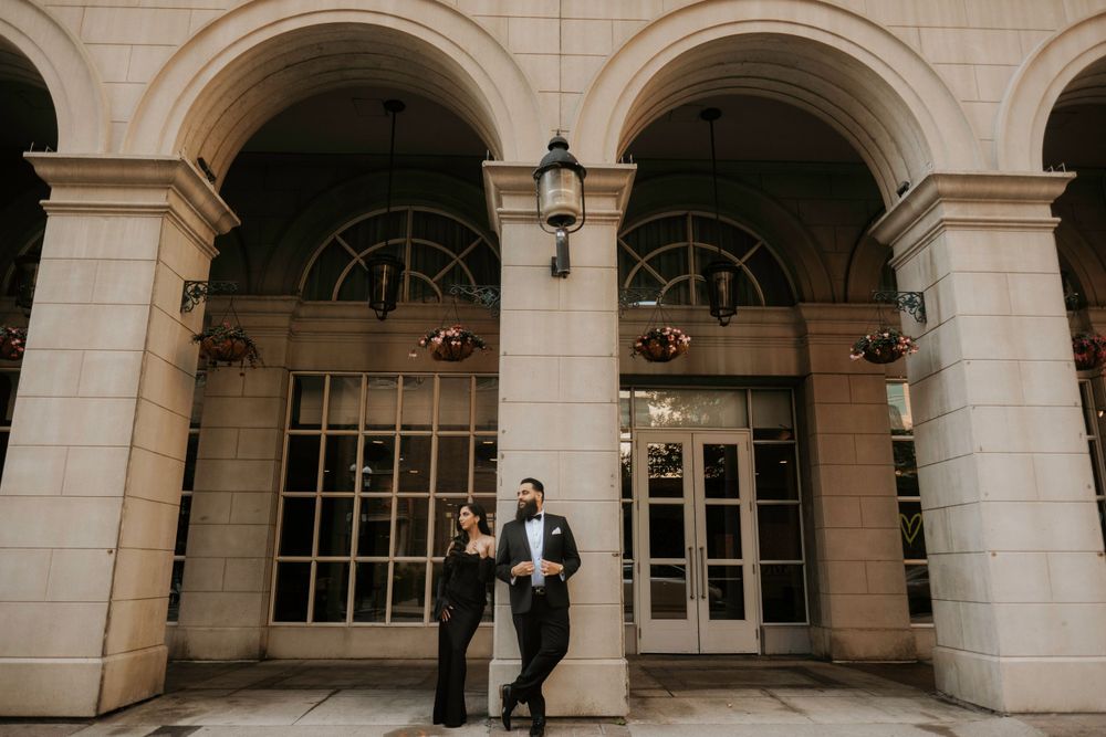 A couple stands together under elegant stone archways with glass doors at a grand entrance.