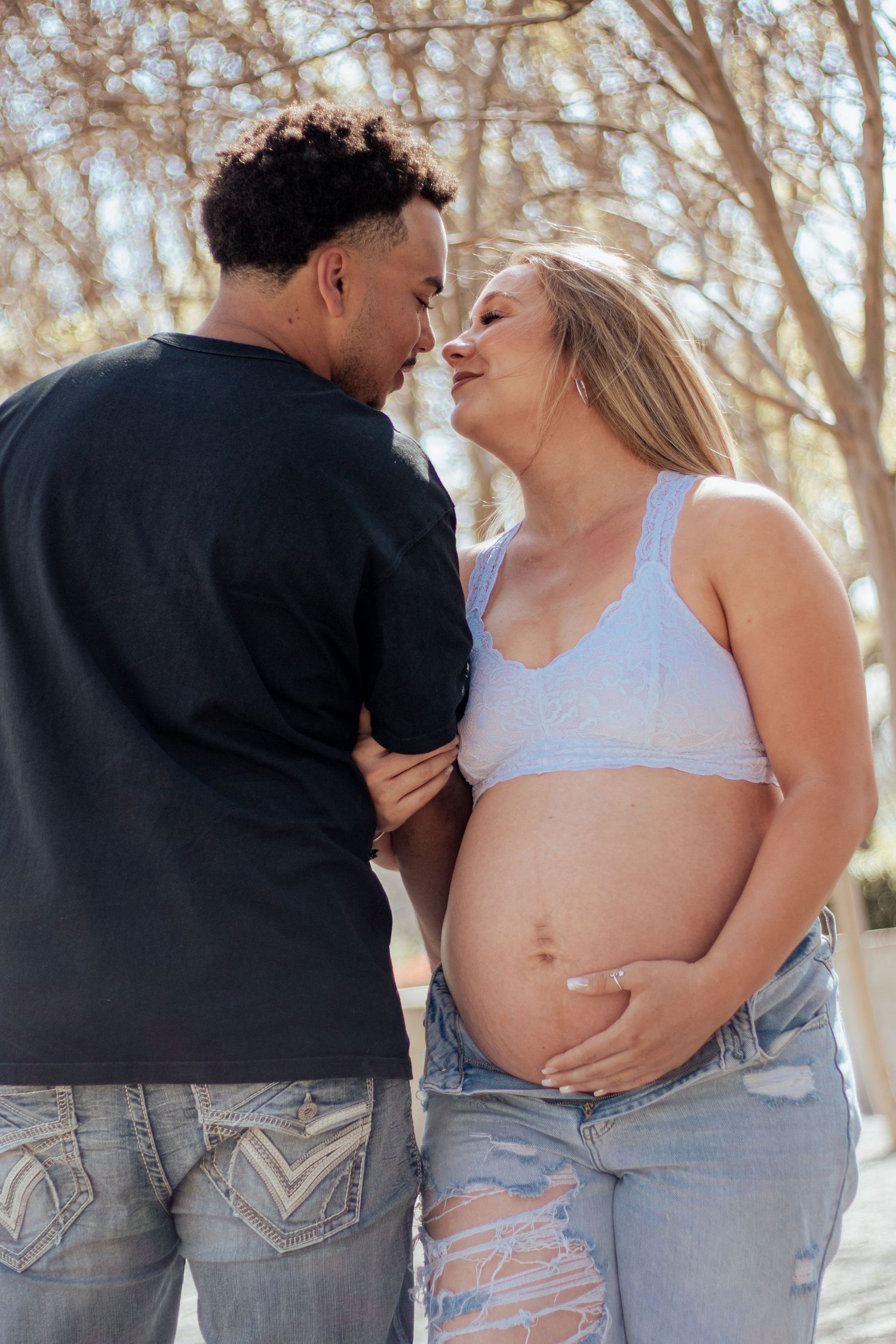 Intimate maternity photo of an expectant couple sharing a tender moment outdoors with trees in the background.