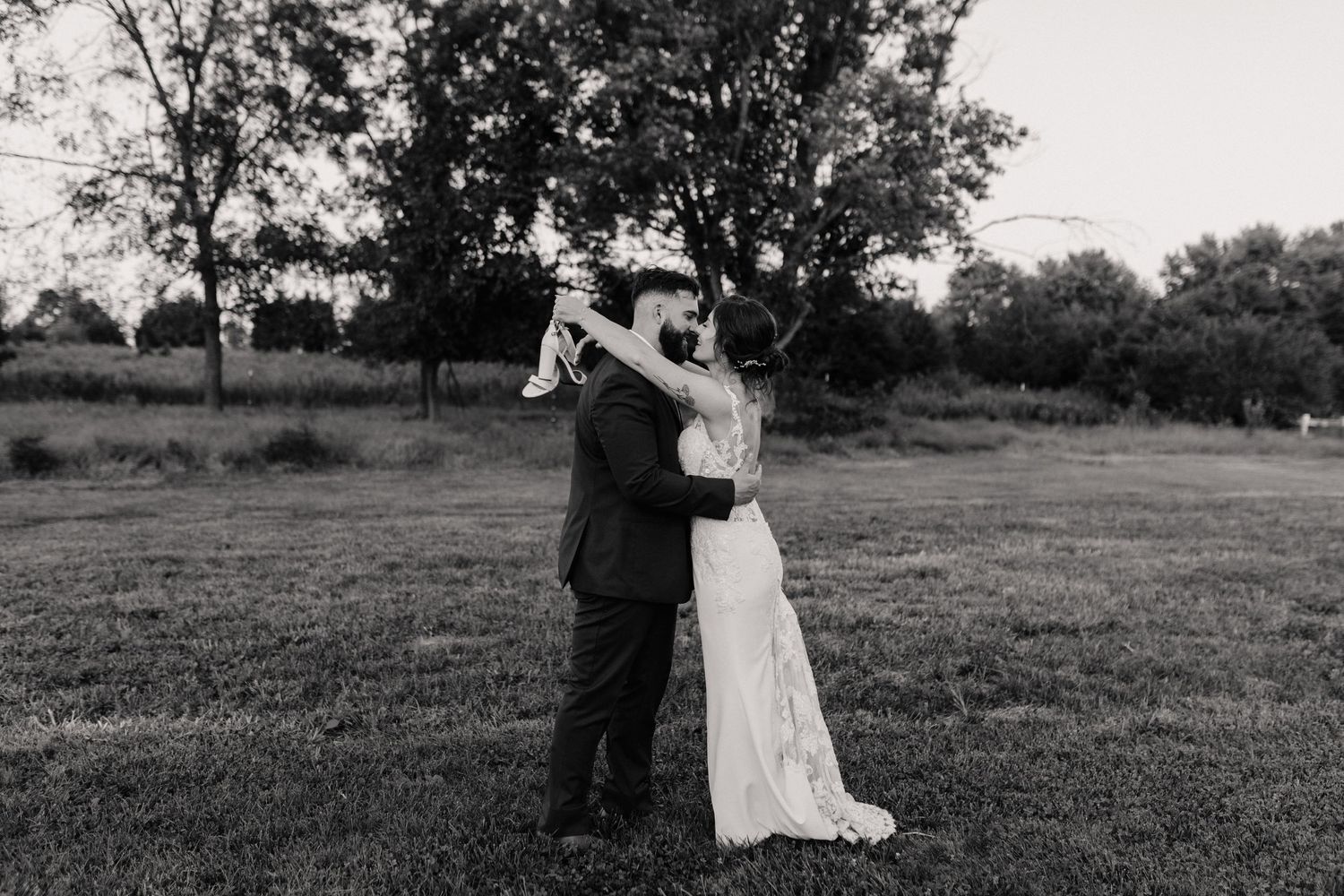 Wedding couple embracing in a serene outdoor field with trees in black and white.