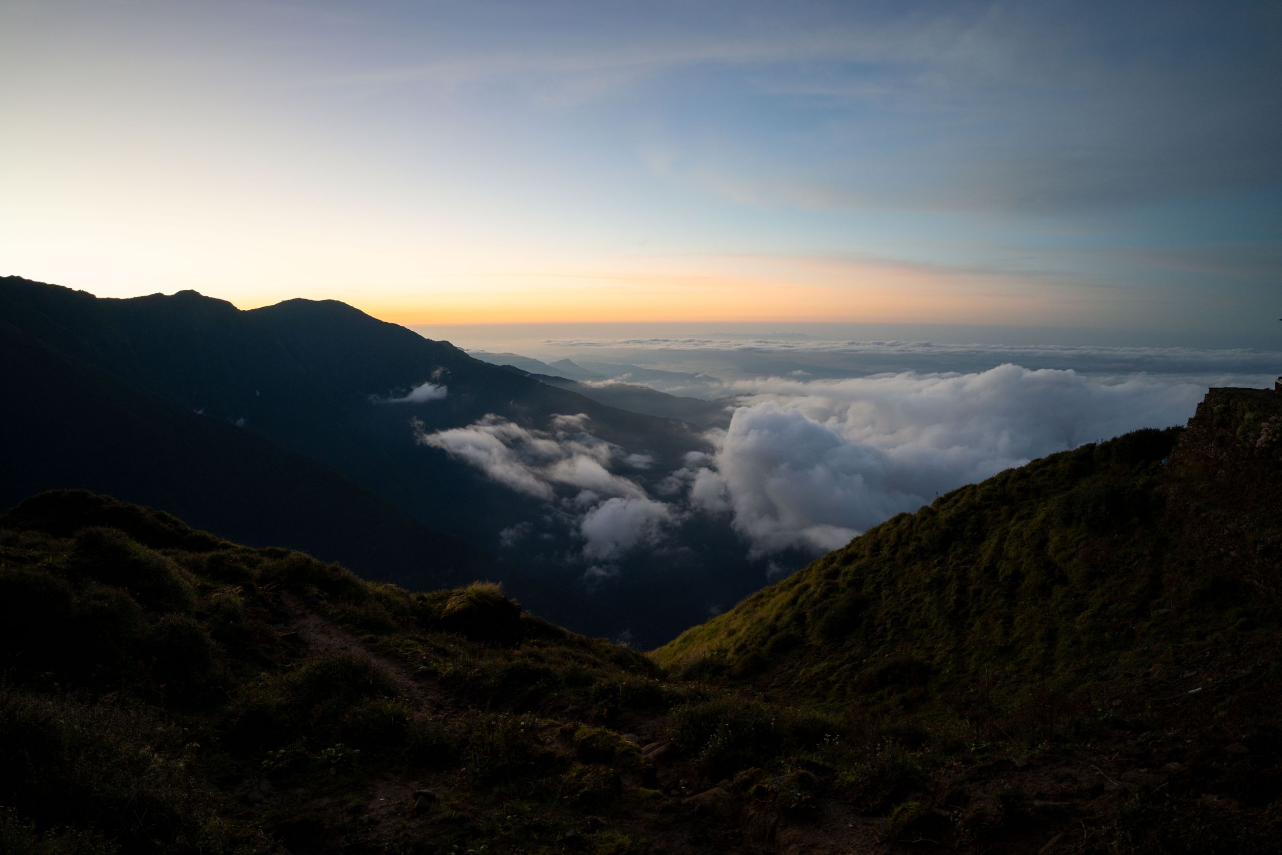 Mountain landscape at dusk with clouds settling in valleys below peaks.