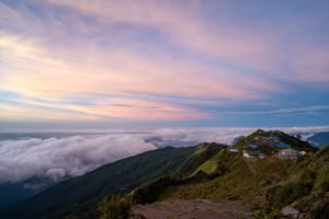 Panoramic mountain vista with clouds rolling over peaks at sunset.