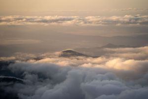 Rolling sea of clouds at sunset with mountain peaks emerging above.