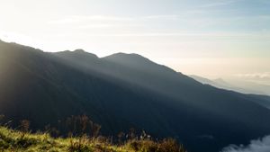 Dramatic mountain ridges silhouetted against evening sky with sunbeams breaking through.