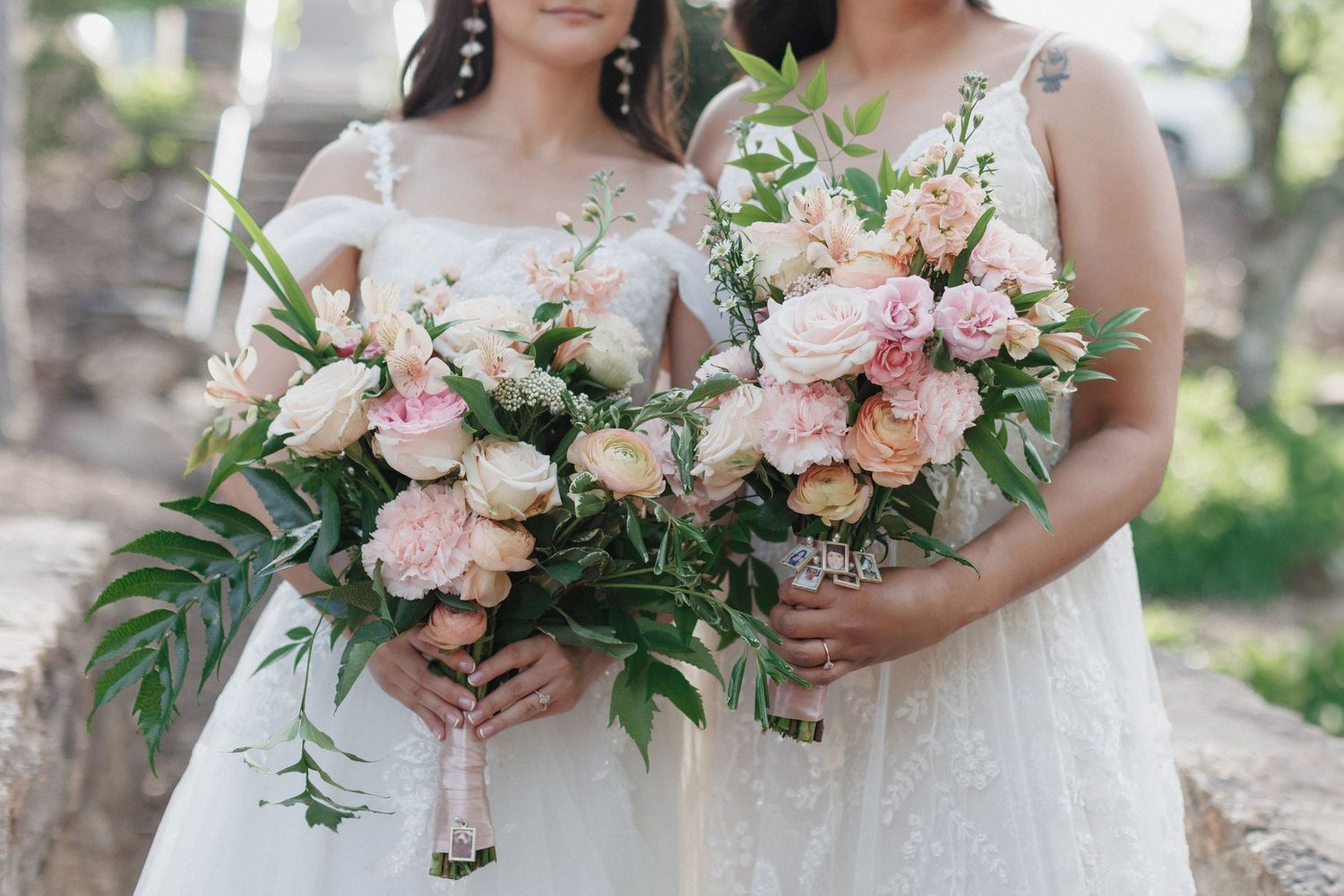 Close-up view of elegant pink and blush floral wedding bouquets with roses and greenery held by figures in soft lighting.
