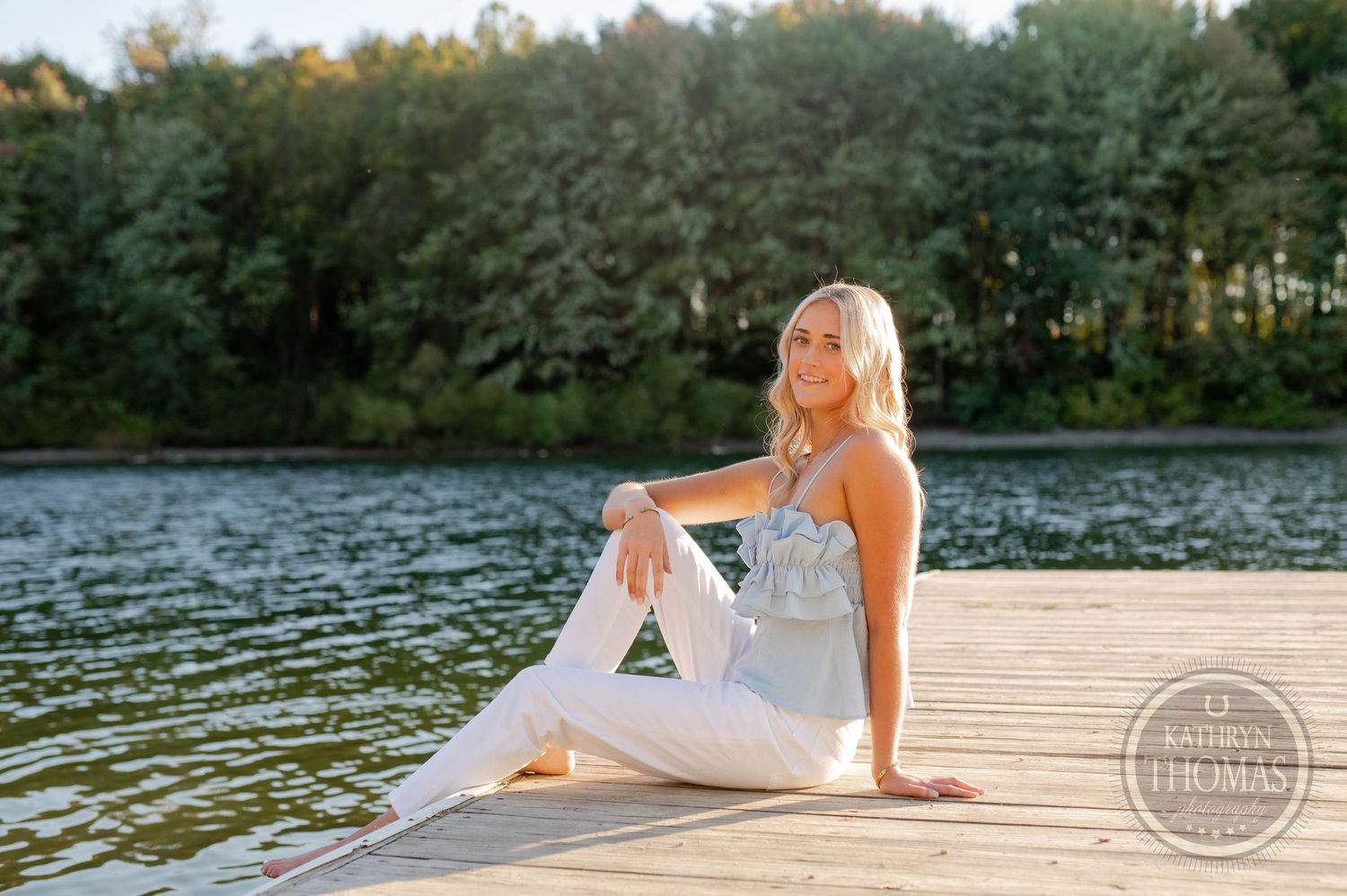 Peaceful lakeside portrait with person in casual attire sitting on wooden dock.