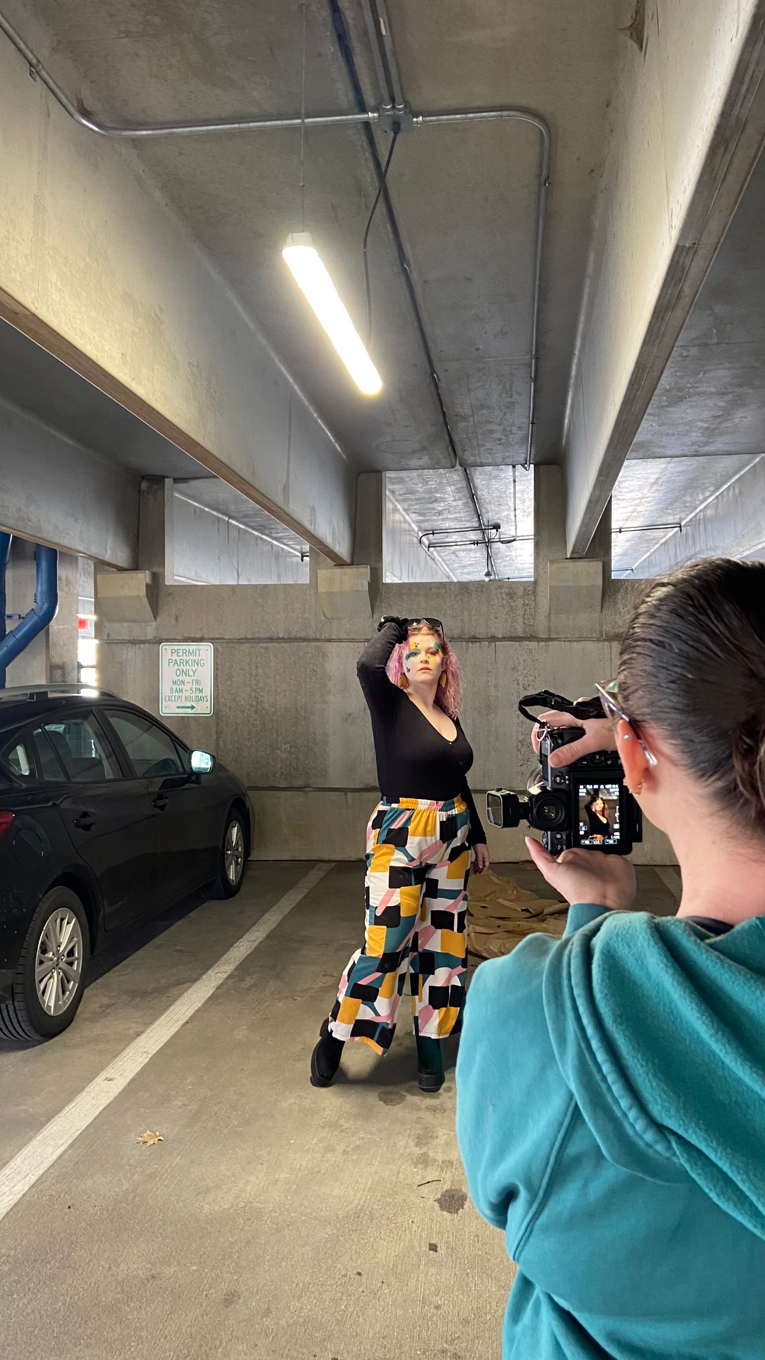 A photography session taking place in a concrete parking garage with colorful patterned pants and professional lighting.
