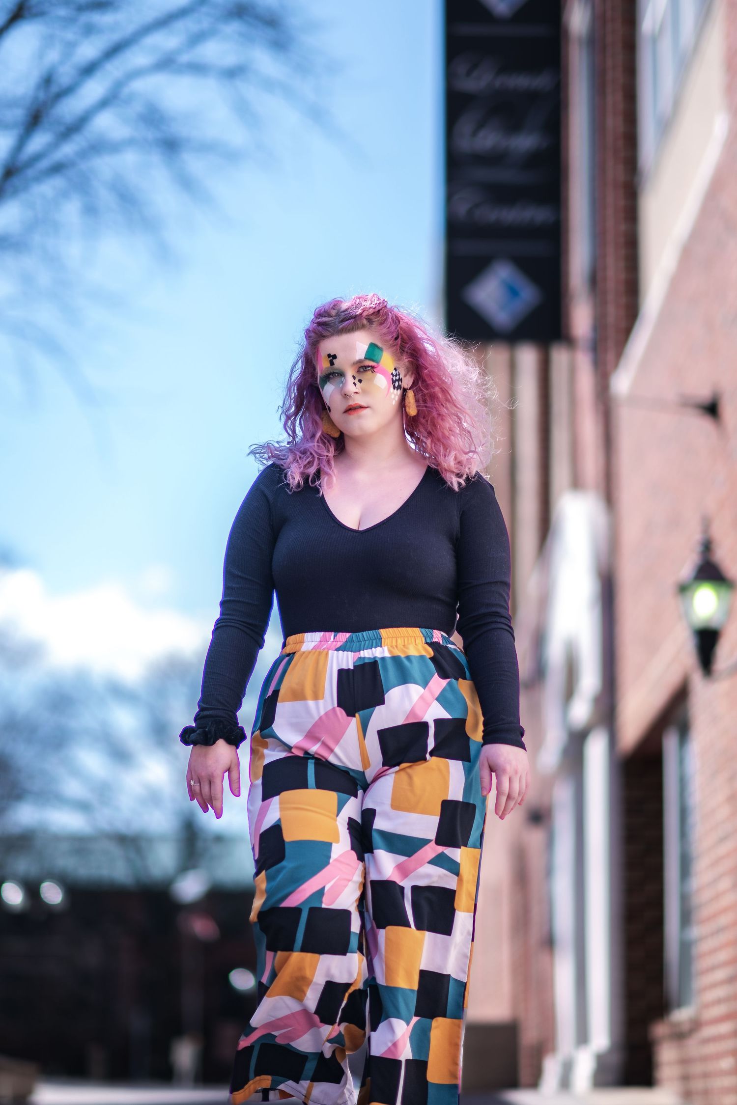 A fashion look featuring colorful geometric print pants paired with a black v-neck top on a city street.