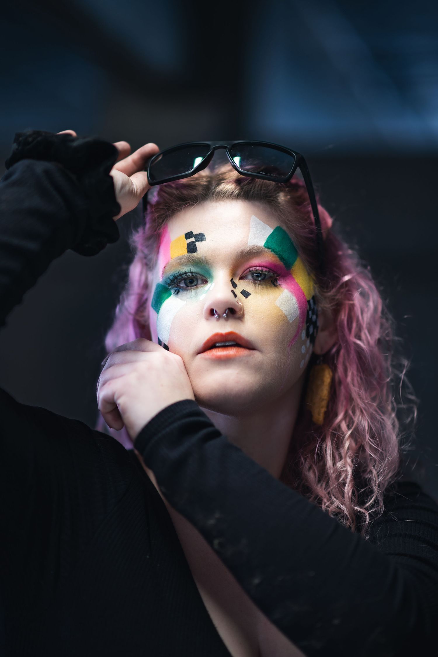 Artistic portrait featuring vibrant rainbow eye makeup, purple hair and black clothing against a dark background.