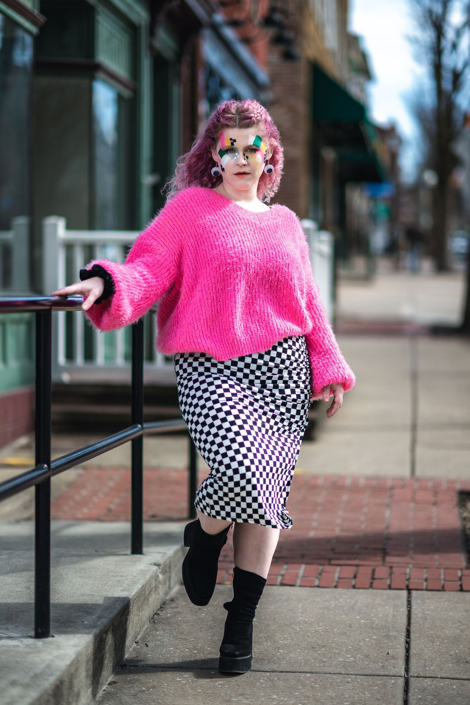 Fashionable street style with bright pink sweater, checkered skirt, black boots and colorful styling on city sidewalk.