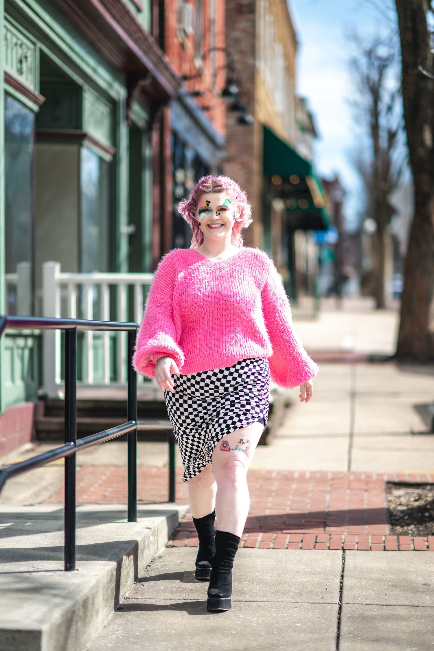 Stylish outfit with pink fuzzy sweater, checkered skirt and black boots on city sidewalk in urban setting.