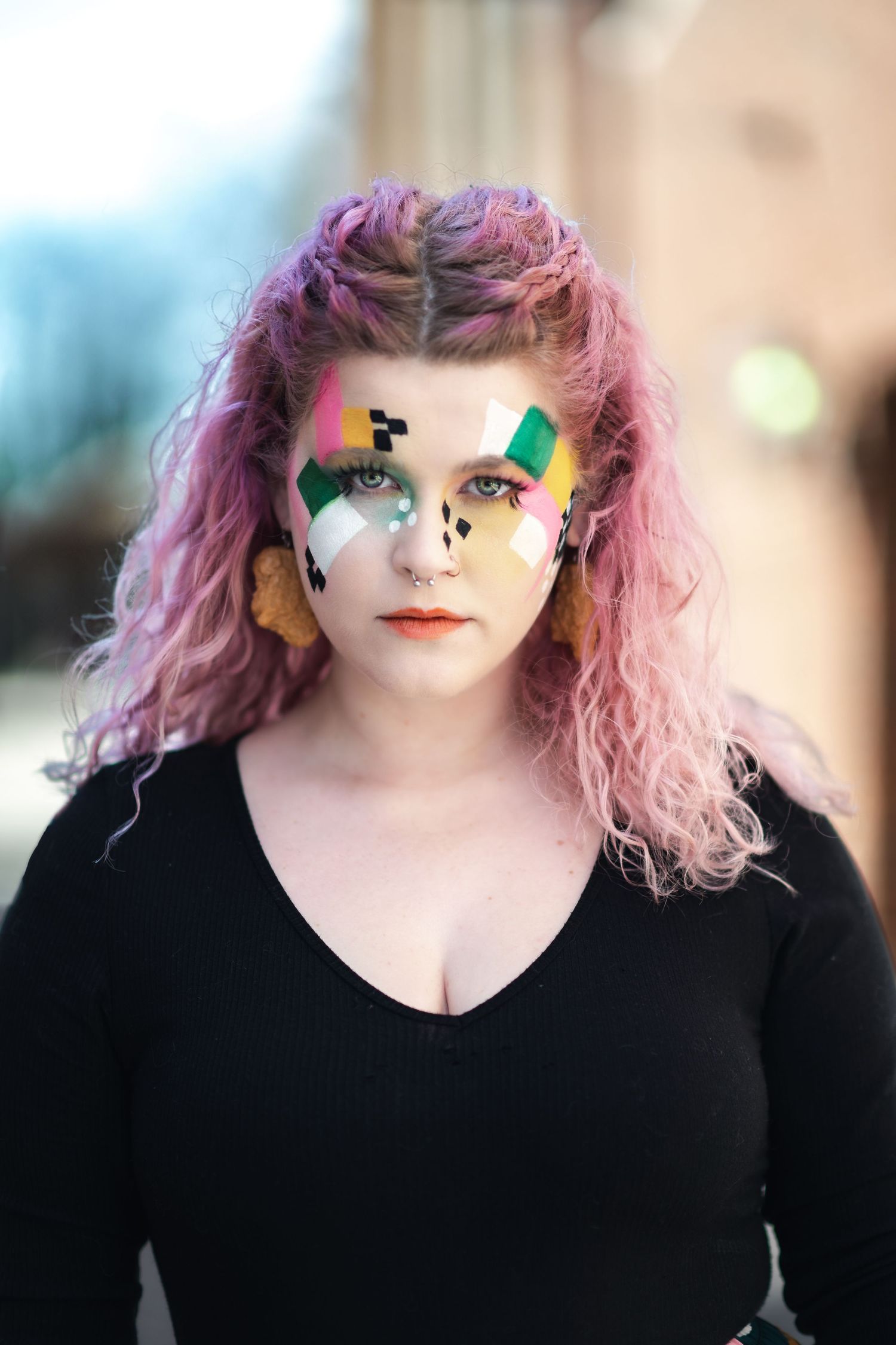Creative portrait showing colorful pride-themed eye makeup and pink wavy hair against blurred background.