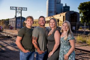 A casual group portrait stands on railroad tracks with a Milwaukee sign and industrial buildings in the background.