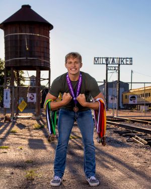 A person stands in front of a historic water tower and Milwaukee railway sign at sunset, holding pride flags.