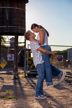 A romantic couple embraces near an old water tower at sunset on a rustic industrial site.